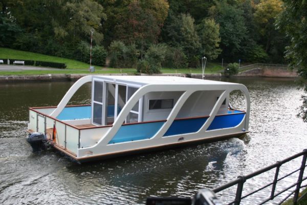 Ein Hausboot in geschwungenem Design bestehend aus GFK-Material, dass auf einem Gewässer unterwegs ist